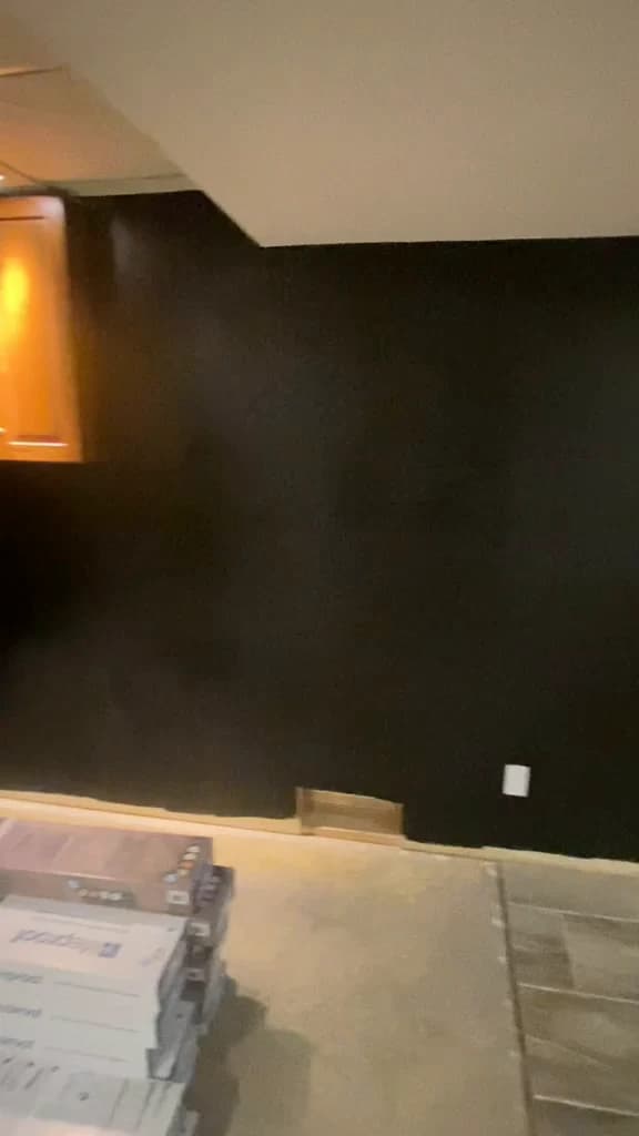 After painting: charcoal basement wall beside the same timber cabinet and unfinished floor