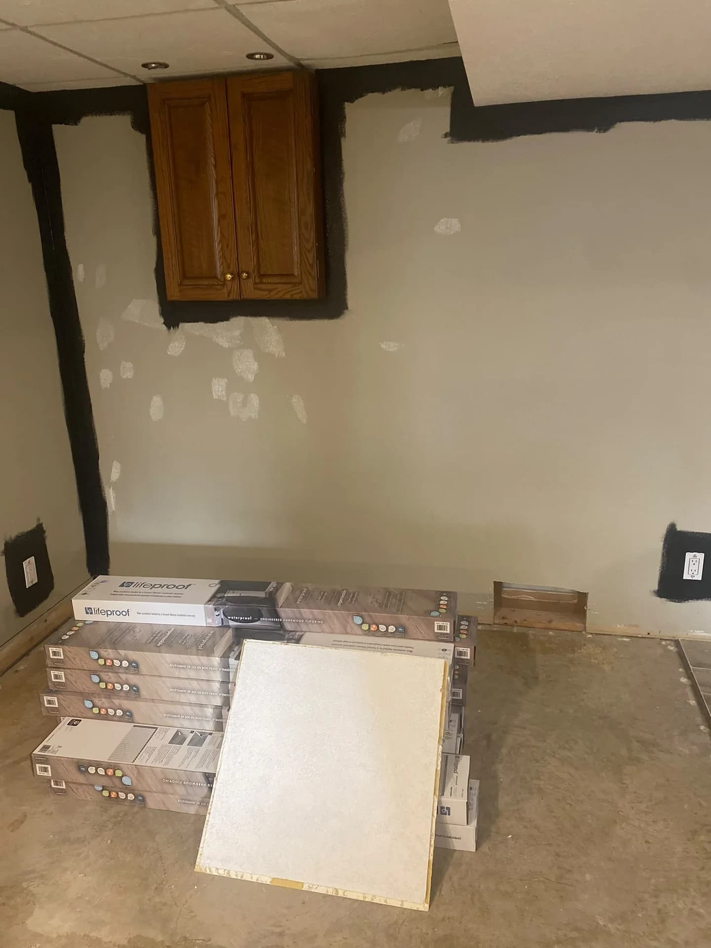 Before final coats: patched basement wall below a wood cabinet, with dark cut-in edges