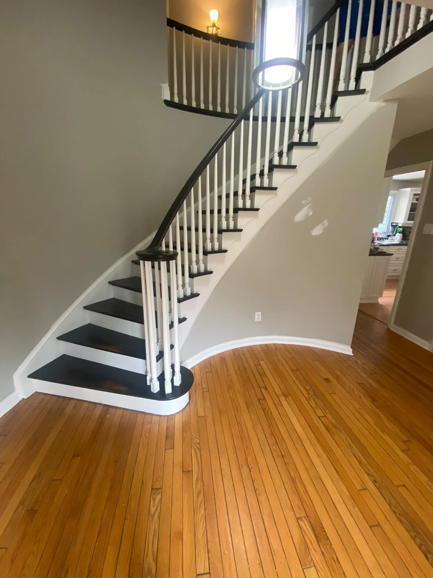 Black and white staircase beside patch-repaired grey walls and a honey-coloured wood floor