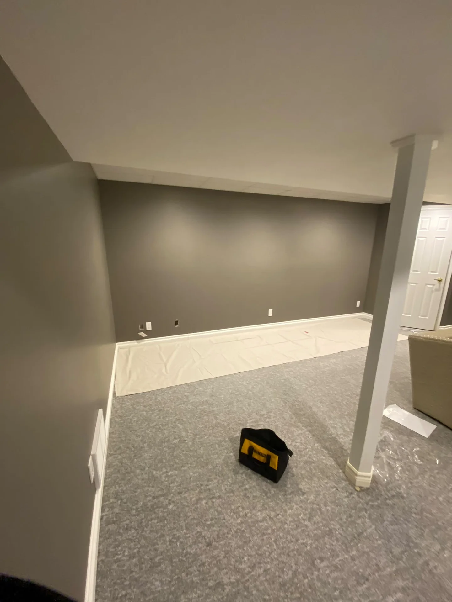 Grey room with a charcoal accent wall, white baseboards and light carpet