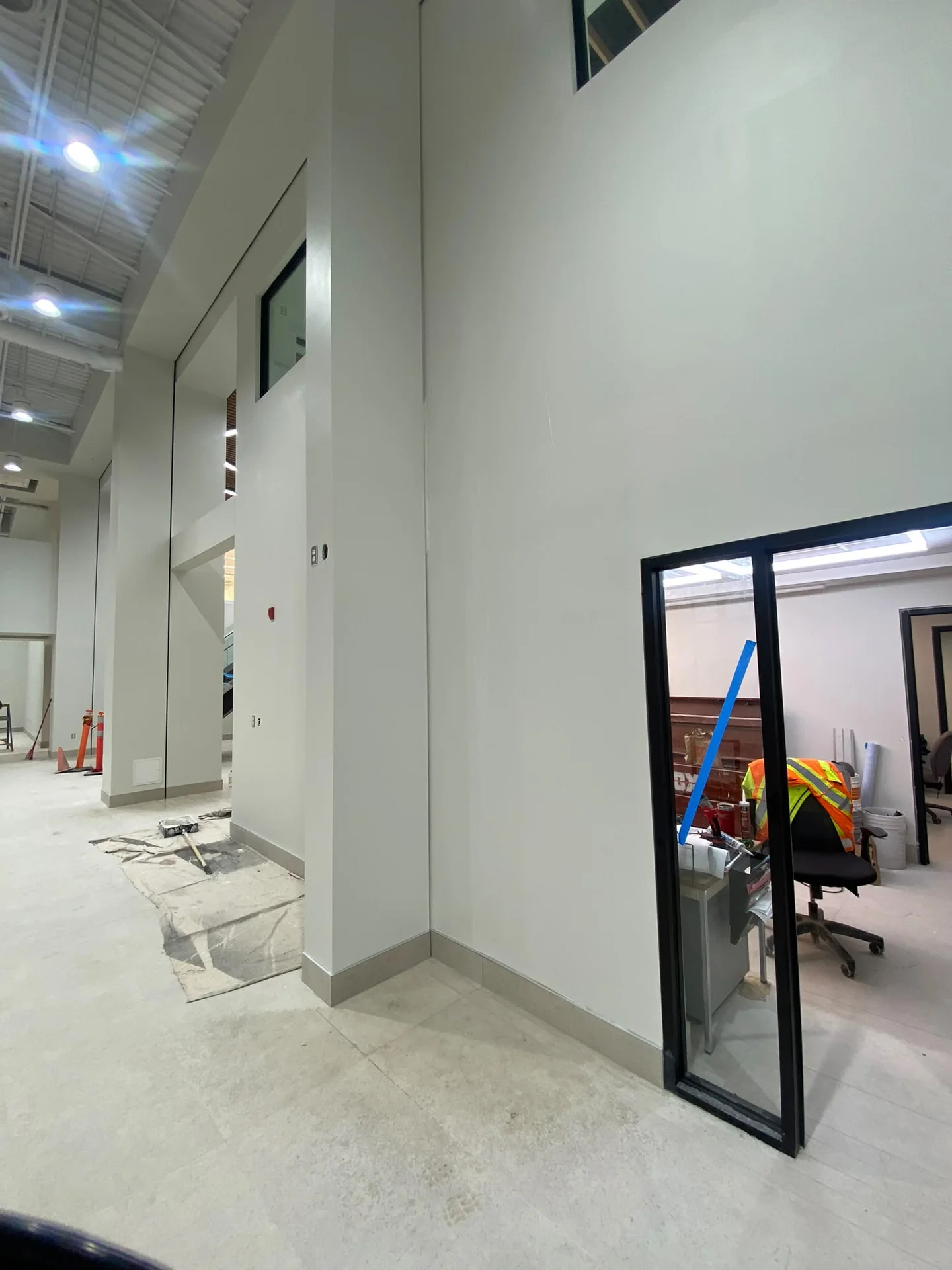 Tall pale commercial corridor walls with an open dark-framed door and protected floor