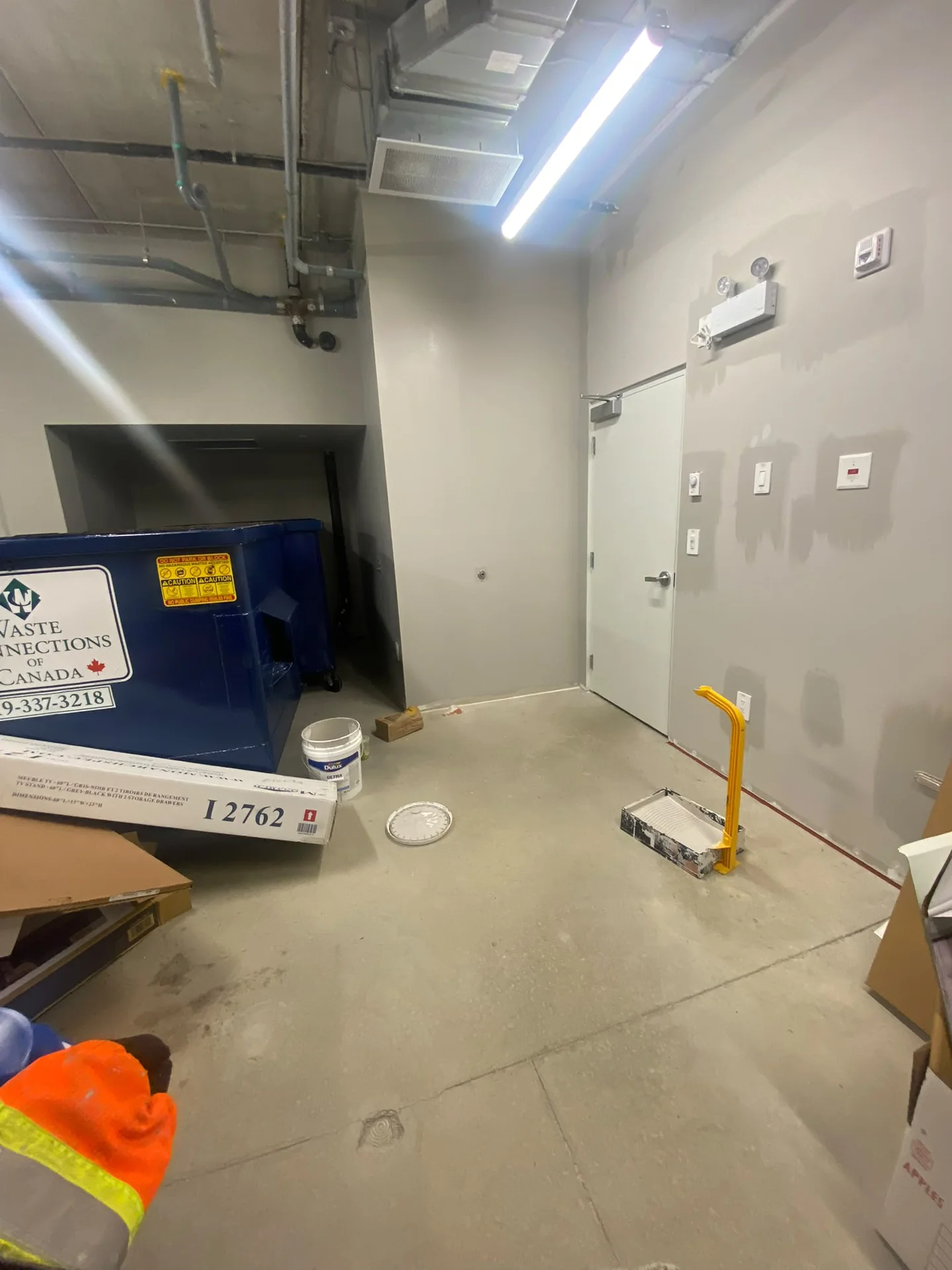 Patched grey wall around utility doors with equipment and floor protection below