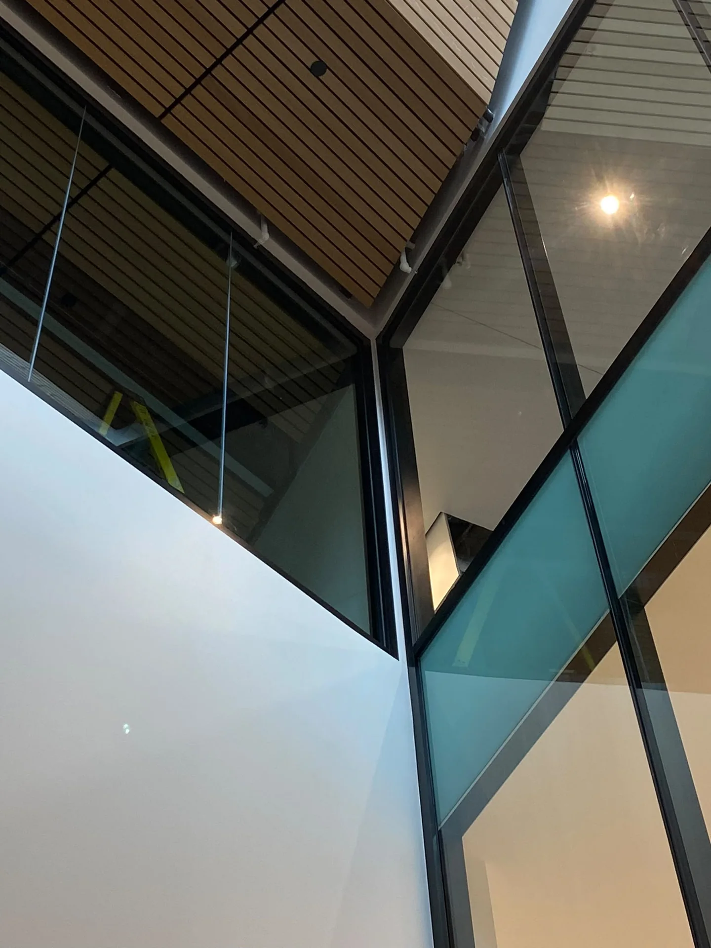 Tall painted wall meeting black-framed glazing and a slatted wood ceiling